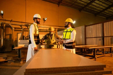 Recording important notes, wooden furniture manufacturing workshop, the concept of discussions and dialogues, two Arab Gulf engineers from Saudi Arabia wearing safety vests and helmets supervising the progress of the work plan, popular crafts and manual professions, carpentry workshops in the Kingdom of Saudi Arabia.