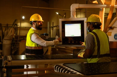 Carpentry workshops in the Kingdom of Saudi Arabia, supervising workers in the workshop, monitoring the workflow, wooden furniture manufacturing factory, industrial professions and jobs, a Gulf Arab Saudi engineer wearing a vest and safety helmet talking to a worker.
