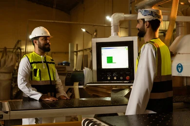 CNC wood router, wood cutting printer, the evolution and technical advancement in traditional industries and crafts, the traditional carpentry profession, laser engraving machine, an Arab Gulf Omani engineer wearing a helmet and safety vest supervising the workflow alongside a colleague.