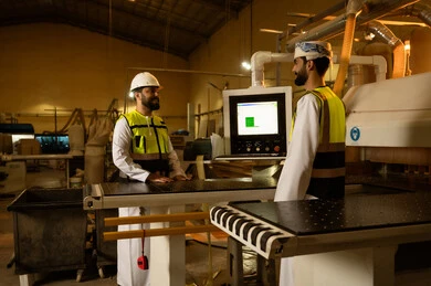 طابعة القطع الخشبية، جهاز توجيه الخشب باستخدام الحاسب الآلي, التطور والتقدم الفني في الصناعات والحرف القديمة, مهنة النجارة التقليدية, آلة النقش بالليزر, مهندس عربي خليجي عماني يرتدي الخوذة وسترة الحماية يقوم بالاشراف على سير خطة العمل برفقة زميلة