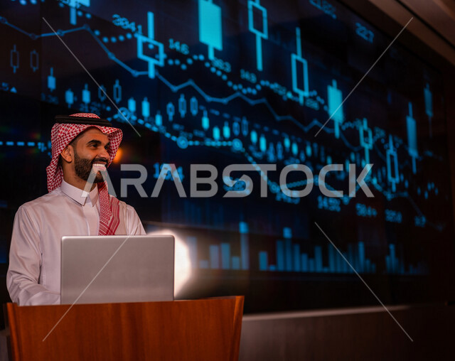 رجل اعمال عربي خليجي سعودي يقف امام الحاسوب المحمول في مؤتمر اقتصادي ، الحديث عن الرسم البياني لسوق الاوراق المالية  ، الاستثمار والنمو الاقتصادي ،تحليل البيانات المالية ، متابعة الاسهم في البورصة ، التطور الاقتصادي السعودي