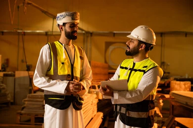 Taking notes through writing, wooden furniture manufacturing workshop, the concept of discussions and dialogues, two Arab Gulf engineers from Oman wearing safety vests and helmets supervising the progress of the work plan, popular crafts and manual professions, carpentry workshops in the Sultanate of Oman.