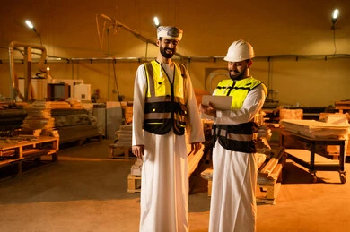 Recording ideas and information, a wooden furniture manufacturing workshop, the concept of discussions and dialogues, two Arab Gulf engineers from Oman wearing safety vests and helmets supervising the progress of the work plan, popular crafts and manual professions, carpentry workshops in the Sultanate of Oman.
