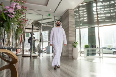 مفهوم السياحه و السفر،  قضاء اوقات ممتعه، ايماءات تدل على الحركة والمشي، التقدم الى الامام، رجل عربي خليجي اماراتي يرتدي الكندورة و الغتره يقوم بالسير داخل الفندق