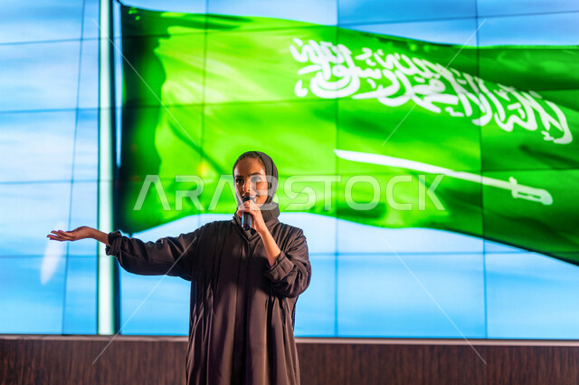 سيدة عربية خليجية سعودية تقف امام خلفية لعلم المملكة العربية السعودية ،حفل الموهوبين السعوديين ، القاء كلمة ترحيبية في مؤتمر سعودي ، الاحتفال باليوم الوطني السعودي ، مؤتمرات و ندوات في السعودية