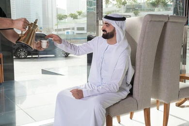 تقديم حسن الضيافة للزوار الكرام داخل الفندق، رجل عربي خليجي اماراتي يرتدي الكندورة و الغتره يقوم بالاستمتاع بتناول مشروب ساخن،  تقديم القهوة العربية الساخنة للسائح في بهو الفندق السياحي ، سياحة وفندقة ، قضاء أجمل الأوقات في أفضل الفنادق الخليجية