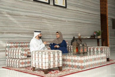 الحديث ومشاركة الأخبار اليومية، تقوية العلاقات الزوجية وروابط الحب والمودة، الاستمتاع بتناول المشروبات الساخنه، مفهوم الاسره السعيده، زوجان عربيان خليجيان اماراتيان يرتديان الزي التقليدي يجلسان فى مجلس شعبي ارضي ، ايماءات السعادة و السرور