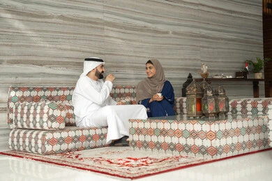 Exchanging news and family conversations, enjoying hot drinks, getting to know each other and building social relationships, the concept of a happy family, an Emirati Gulf Arab couple wearing traditional attire sitting in a ground-level popular gathering, gestures of happiness and joy.
