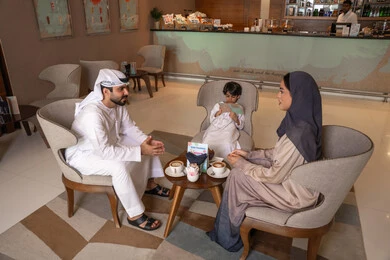 تبادل المعلومات والمناقشات، الاستمتاع بتناول المشروبات الساخنه، تعارف وبناء علاقات اجتماعيه، مفهوم الاسره السعيده، زوجان عربيان خليجيان اماراتيان يرتديان الزي التقليدي يجلسان في كافية برفقة ابنهم