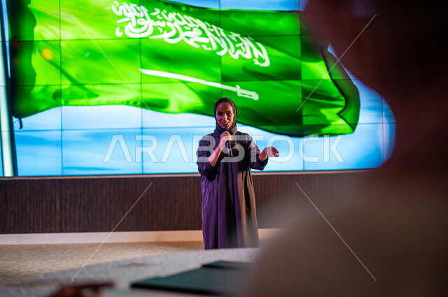 سيدة عربية خليجية سعودية تقف امام خلفية لعلم المملكة العربية السعودية ،حفل الموهوبين السعوديين ، القاء كلمة ترحيبية في مؤتمر سعودي ، الاحتفال باليوم الوطني السعودي ، مؤتمرات و ندوات في السعودية