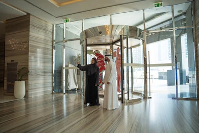 The concept of a happy family, a weekend getaway, an enjoyable couple's trip, spending the best times in the best Gulf hotels, an Emirati Arab couple dressed in traditional attire standing in the lobby of a tourist hotel, pointing to something.
