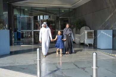 The concept of tourism and travel, an Arab Gulf Emirati man wearing a kandura and ghutrah walking outside the hotel with his wife and daughter, spending an enjoyable summer vacation, creating happy moments with the family.
