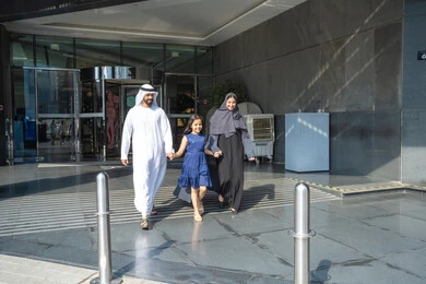 Spending happy moments with the family, enjoying a fun summer vacation, an Emirati Gulf Arab man wearing a kandura and ghutrah walking outside the hotel with his wife and daughter, the concept of tourism and travel.