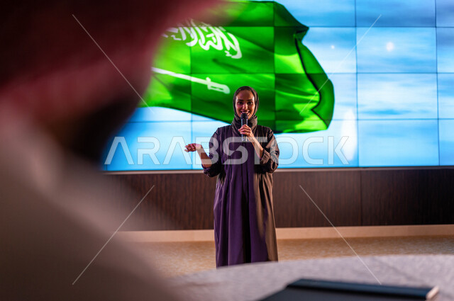 سيدة عربية خليجية سعودية تقف امام خلفية لعلم المملكة العربية السعودية ،حفل الموهوبين السعوديين ، القاء كلمة ترحيبية في مؤتمر سعودي ، الاحتفال باليوم الوطني السعودي ، مؤتمرات و ندوات في السعودية