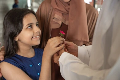 اهتمام الوالدين بصحة وسعادة الأبناء، قضاء أوقات سعيدة برفقة الأهل، ايماءات السعادة و السرور، رجل عربي خليجي اماراتي يرتدي الكندورة و الغتره يقف برفقة زوجته فى مدخل اسقبال الفندق يقوم بتقديم وردة الي ابنته، الاستعداد لقضاء رحلة سياحية ممتعه مع العائلة