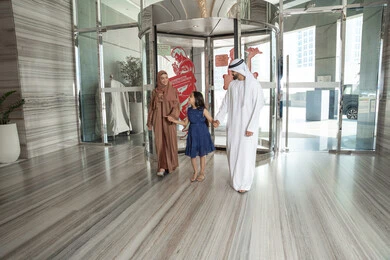 The concept of tourism and travel, enjoying spending time with family, an Emirati Gulf Arab family dressed in traditional attire walking into the hotel reception area, preparing to have an enjoyable tourist trip with the family, exchanging conversations with expressions of joy and happiness.