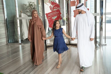 عائلة عربيه خليجيه اماراتية ترتدي الزي التقليدي يسيرون داخل مدخل الاستقبال فى الفندق، الاستعداد لقضاء رحلة سياحية ممتعه مع العائلة، تبادل الاحاديث بتعابير السرور و السعادة, الاستمتاع في قضاء الوقت مع الأهل