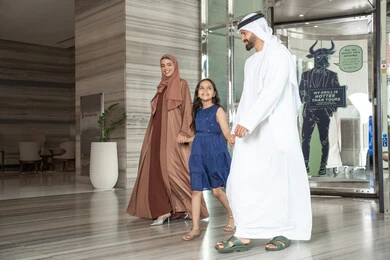 Getting ready for an enjoyable family trip, exchanging conversations with expressions of joy and happiness, an Emirati Gulf Arab family dressed in traditional attire walking into the hotel reception, enjoying spending time with family.