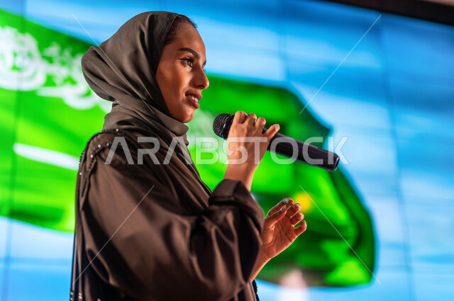 سيدة عربية خليجية سعودية تقف امام خلفية لعلم المملكة العربية السعودية ،حفل الموهوبين السعوديين ، القاء كلمة ترحيبية في مؤتمر سعودي ، الاحتفال باليوم الوطني السعودي ، مؤتمرات و ندوات في السعودية