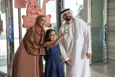 Family moments filled with happiness, a Gulf Arab Emirati man wearing the kandura and dishdasha stands with his wife and daughter, gesturing with joy and delight, pointing to something, moments of an Emirati Gulf Arab family entering a tourist hotel. Family moments filled with happiness, a Gulf Arab Emirati man wearing the kandura and dishdasha stands with his wife and daughter, gesturing with joy and delight, pointing to something, moments of an Emirati Gulf Arab family entering a tourist hotel.