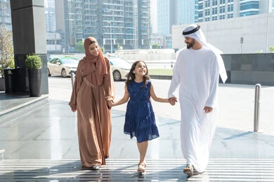 The concept of tourism during the summer vacation, an Emirati Arab couple wearing traditional attire walking in front of the hotel with their daughter, having a good time, preparing to travel on a sightseeing tour, enjoying a fun and entertaining summer trip.