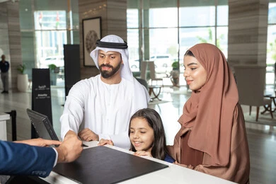 تأكيد بيانات الحجز في المنتجع، الاستمتاع بالعطلة الصيفية، رجل اماراتي يرتدي الكندورة و الغتره يقف برفقة زوجته و ابنته عند مكتب الاستقبال فى احد الفنادق الفاخره، تعابير السعادة و السرور