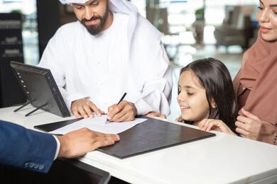 Weekend, a close-up shot of an Emirati man wearing a kandura and ghutrah standing with his wife and daughter at the reception desk of a luxury hotel confirming his reservation at the resort, expressions of happiness and joy.