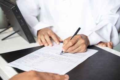 Spending a happy summer vacation, a close-up shot of the hand of an Arab Gulf Emirati man wearing a kandura standing at the reception desk in a luxury hotel confirming his reservation at the resort.