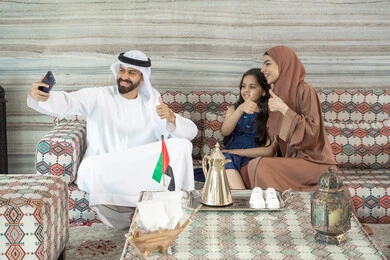 مفهوم القبول والموافقه، أنشطة ترفيهية مع الأسرة، رجل عربي خليجي اماراتي يرتدي الكندورة و الغتره يجلس فى مجلس ارضي شعبي برفقة زوجته و ابنته يقوم بالتقاط صور السيلفي عبر الهاتف المحمول ، تعابير السعادة و السرور مفهوم القبول والموافقه، أنشطة ترفيهية مع الأسرة، رجل عربي خليجي اماراتي يرتدي الكندورة و الغتره يجلس فى مجلس ارضي شعبي برفقة زوجته و ابنته يقوم بالتقاط صور السيلفي عبر الهاتف المحمول ، تعابير السعادة و السرور