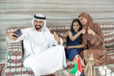 إشارات بالموافقة والإيجاب، أنشطة ترفيهية مع الأسرة، مفهوم الأسرة السعيدة، رجل عربي خليجي اماراتي يرتدي الكندورة و الغتره يجلس فى مجلس ارضي شعبي برفقة زوجته و ابنته يقوم بالتقاط صور السيلفي عبر الهاتف المحمول ، تعابير السعادة و السرور إشارات بالموافقة والإيجاب، أنشطة ترفيهية مع الأسرة، مفهوم الأسرة السعيدة، رجل عربي خليجي اماراتي يرتدي الكندورة و الغتره يجلس فى مجلس ارضي شعبي برفقة زوجته و ابنته يقوم بالتقاط صور السيلفي عبر الهاتف المحمول ، تعابير السعادة و السرور