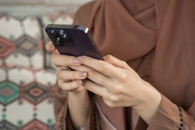 Chatting with family and friends, using modern technological devices, a close-up shot of the hand of an Arab Gulf Emirati woman holding a mobile phone browsing social media.