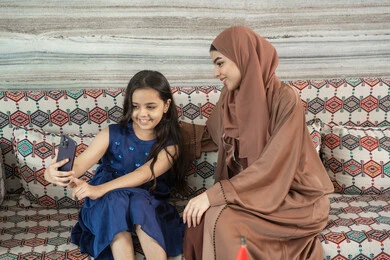 توثيق أجواء عائلية سعيدة من خلال سيلفي، فرحة الأبناء بقضاء وقت ممتع مع الأهل, بنت عربيه خليجيه اماراتية ترتدي الفستان تجلس فى مجلس ارضي شعبي تقوم بتوثيق اللحظات الممتعة مع  والدتها، ايماءات السعادة و السرور