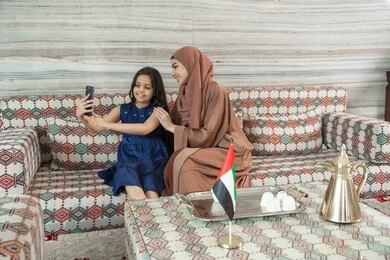 أخذ صورة تذكارية عائلية باستخدام الجوال، فرحة الأبناء بقضاء وقت ممتع مع الأهل, بنت عربيه خليجيه اماراتية ترتدي الفستان تجلس فى مجلس ارضي شعبي تقوم بتوثيق اللحظات الممتعة مع  والدتها، ايماءات السعادة و السرور