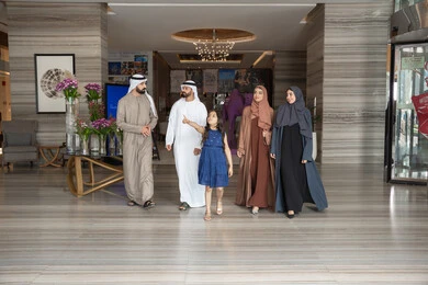 الاشارة الي شيء ما، الاستمتاع باللحظات الأسرية السعيدة، الاستعداد لقضاء رحلة سياحية ممتعه مع العائلة، تبادل الاحاديث بتعابير السرور و السعادة,عائلة عربيه خليجيه اماراتية ترتدي الزي التقليدي يسيرون داخل مدخل الاستقبال فى الفندق