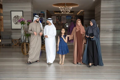 الاستمتاع في قضاء الوقت مع الأهل، الاستعداد لقضاء رحلة سياحية ممتعه مع العائلة، تبادل الاحاديث بتعابير السرور و السعادة,عائلة عربيه خليجيه اماراتية ترتدي الزي التقليدي يسيرون داخل مدخل الاستقبال فى الفندق