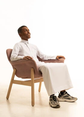 مفهوم الراحة والاسترخاء, الشعور بالتعب والخمول، الاستمتاع بالأجواء الهادئة,  بورتريه لرجل عربي خليجي سعودي مبتسم يرتدي الثوب التقليدي يجلس على كرسي مريح بتعابيرالراحة، خلفية بيضاء