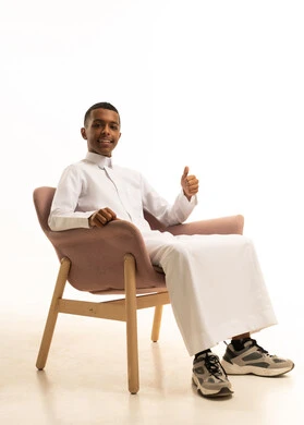 A portrait of a smiling Saudi Gulf Arab man wearing traditional attire sitting on a comfortable chair with expressions of relaxation, enjoying the calm atmosphere, the concept of comfort and relaxation, feeling tired and lethargic, with a white background.