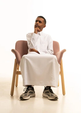 بورتريه لشاب مراهق عربي خليجي سعودى يرتدي الثوب التقليدى يجلس على كرسي مريح ويضع يده على خده بتعابير التفكير و التأمل، محاولة إيجاد حل مشكلة، التمعن والتركيز والتخطيط للمستقبل، شرود الذهن إلى مكان ما, النظر بعيداً لتذكر شيء، إيماءات الحيرة والقلق، خلفية بيضاء