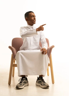 Pointing with the index finger at something, the concept of elegance, masculinity, and concern for appearance, a portrait of a young Arab Gulf Saudi teenager wearing traditional attire, smiling while sitting on a comfortable chair, looking at the camera with expressions of joy and happiness, white background. Pointing with the index finger at something, the concept of elegance, masculinity, and concern for appearance, a portrait of a young Arab Gulf Saudi teenager wearing traditional attire, smiling while sitting on a comfortable chair, looking at the camera with expressions of joy and happiness, white background.