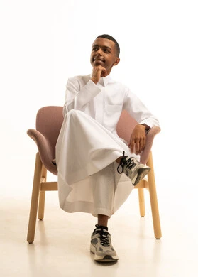 تعابير التفكير والتأمل، بورتريه لشاب مراهق عربي خليجي سعودى يرتدي الثوب التقليدى يجلس على كرسي مريح ويضع يده على خده ،محاولة إيجاد حل مشكلة، التمعن والتركيز والتخطيط للمستقبل، شرود الذهن إلى مكان ما, إيماءات الحيرة والقلق، خلفية بيضاء