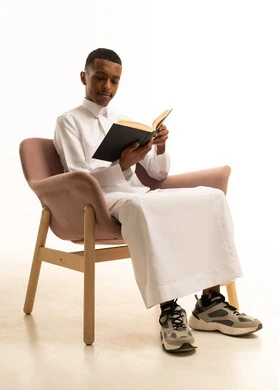 تطوير المناهج التعليمية في السعودية، مراجعة الدروس للمذاكرة والاختبارات المدرسية، تعابير الاجتهاد والتفوق, بورتريه لشاب مراهق عربي سعودى يرتدي الثوب التقليدى يجلس على كرسي مريح يمسك بيده الكتاب المدرسي، ايماءات التركيزوالتفكير، خلفية بيضاء