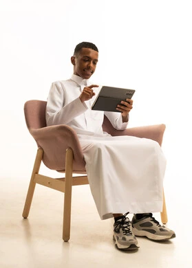 Research and reading through applications, browsing social media, using modern and advanced devices and technologies, a portrait of a smiling young Arab Gulf Saudi man wearing traditional attire using a tablet, white background.