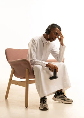 تعابير تدل على الخسارة والهزيمة، بورتريه لشاب عربي خليجي سعودي يرتدي الثوب التقليدي يجلس على كرسى يضع سماعة الرأس يمسك بيده عصا التحكم عن بعد، خلفية بيضاء