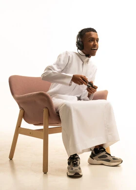 إيماءات وجه ويدين مختلفة تدل على الذهول والحماس، إستخدام أجهزة تقنية حديثة، بورتريه لشاب عربي خليجي سعودي مبتسم يرتدي الثوب التقليدي يضع سماعة الرأس يمسك بيده عصا التحكم عن بعد، خلفية بيضاء