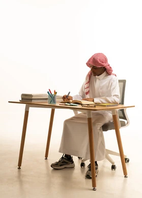 Education and teaching with the prescribed curricula for students in the Kingdom of Saudi Arabia, a portrait of a Gulf Arab Saudi student wearing a white thobe and a shemagh solving school assignments, white background.