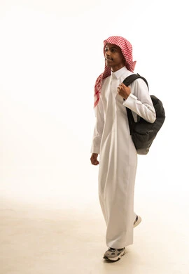 بورتريه من الجانب لطالب عربي خليجي سعودي يرتدي الثوب التقليدي والشماغ  يحمل حقيبة الظهر المدرسية ينظر للكاميرا بإيماءات السرور والسعادة، الوقوف بظهر مشدود واستقامة، موسم العودة إلى المدارس، الجسم بالطول الكامل، خلفية بيضاء