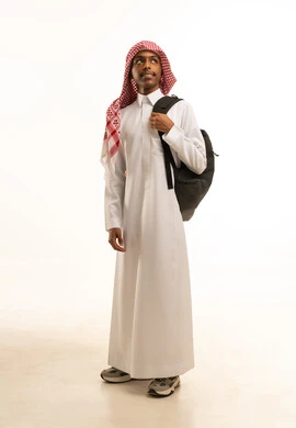 A portrait of a smiling Saudi Gulf Arab student wearing traditional attire and a shemagh, with a backpack, looking at something, preparing for the start of the new school year, full-body image, white background.