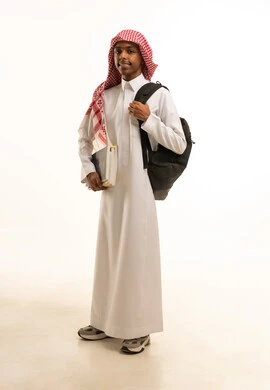 المدارس التعليمية في المملكة السعودية ، بورتريه لطالب عربي خليجي سعودي مبتسم يرتدي الثوب التقليدي والشماغ وحقيبة ظهر ينظر الى الكاميرا، صورة الجسم بالطول الكامل، خلفية بيضاء