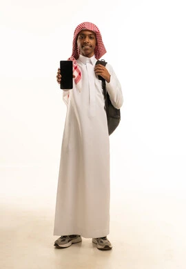 استخدام الأجهزة والتقنيات الحديثة والمتطورة, البحث والمطالعة من خلال الجوال، تصفح التطبيقات ووسائل التواصل الاجتماعي، بورتريه لشاب عربي خليجي سعودي مبتسم يرتدي الثوب التقليدي و الشماغ وحقيبة ظهر يحمل بيده الهاتف المحمول بشاشة سوداء فارغة , خلفية بيضاء