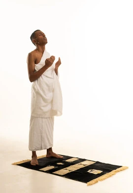 The concept of the pillars of Islam and religious obligations, performing the rituals of Hajj and Umrah, a portrait of a young Gulf Arab Saudi man wearing Ihram clothing standing upright, raising his hands to the sky, praying with gestures of supplication and humility, rituals of Hajj and Umrah, white background.